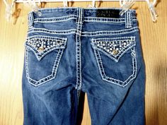 Get ready to shine in these designer VIGOSS Jeans! The dark wash and bootcut leg are perfect for any season. The blingy rhinestone gems and flap pockets add a touch of western flair to your wardrobe. Made with stretchy, breathable, and slimming material, these jeans will become your new favorite. #VigossJeans #BlingyJeans #DesignerDenim #WesternStyle #RhinestoneGems #FlapPockets Rhinestone Jean Pockets, Lowrise Rhinestone Jeans, Dark Wash Denim Jeans With Rhinestones, Embellished Fitted Dark Wash Jeans, Denim Rhinestone-embellished Short Bottoms, Vigoss Jeans