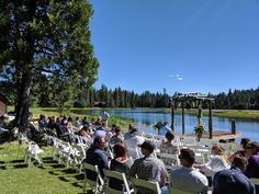 people are sitting on white chairs at the edge of a lake while others sit in front of them