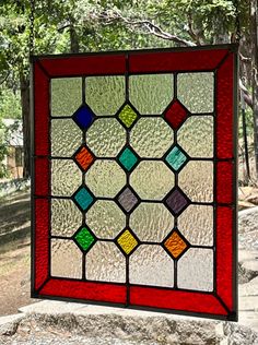 a colorful stained glass window sitting on top of a stone slab in front of trees