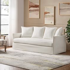 a living room with white furniture and paintings on the wall, along with a rug