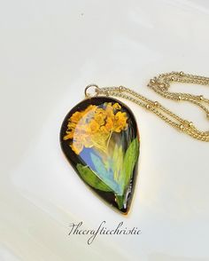 a yellow flower is sitting on top of a black heart shaped pendant with gold chains