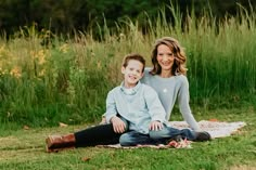 a woman and boy are sitting on a blanket in the grass smiling at the camera