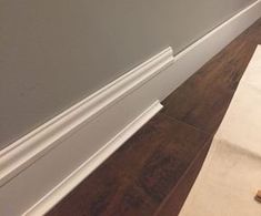 a room with white trim and wood flooring next to a wall that has been painted gray