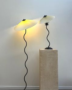 two lamps sitting next to each other on top of a cement block in front of a white wall