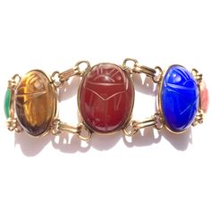 Looking for colorful jewelry? A go with everything good luck bracelet? This vintage scarab bracelet has seven gorgeous semi precious stones, set in 12K gold filled open bezels with double links in between. Gemstone scarabs are are a very nice size. This eye catching gold filled bracelet stands out all on its own! Era: Mid Century. Bracelet is 7.25 inches long by 0.8 inches wide. Scarabs with their settings are 21.5mm by 16.5mm.  Marks: Hallmark, 1/20 12K G. F., hallmark. Gemstones from spring ri Heirloom Multicolor Oval Jewelry, Antique Multi-stone Bracelets As Gift, Antique Multi-stone Bracelet As Gift, Classic Multicolor Gemstone Jewelry, Multicolor Cabochon Costume Jewelry, Gold Multi-stone Oval Cabochon Jewelry, Gold Oval Cabochon Multi-stone Jewelry, Vintage Multicolor Cabochon Jewelry, Heirloom Multicolor Jewelry For Gifts