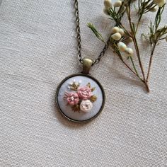 a necklace with flowers on it sitting next to a flower vase and some white flowers