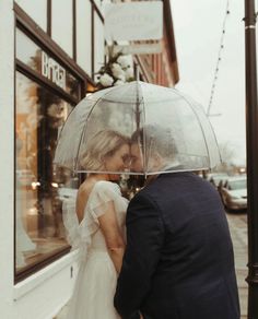 a bride and groom standing under an umbrella on the sidewalk in front of a store