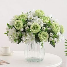 a vase filled with white and green flowers on top of a table next to a cup