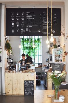 the interior of a coffee shop with menus on the wall and plants hanging from the ceiling