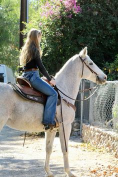 a woman riding on the back of a white horse