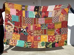 two people holding up a multicolored quilt