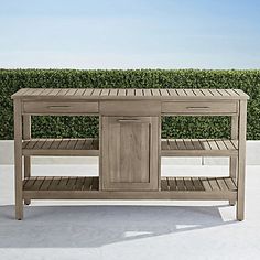 a wooden table sitting on top of a white floor next to a hedge covered wall