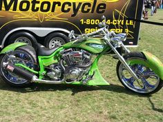 a green motorcycle parked next to a black and yellow truck on top of a grass covered field