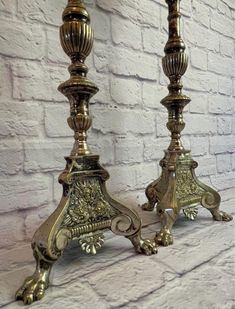 two metal candlesticks sitting next to each other on a white brick wall background