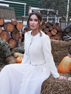 a woman sitting on hay with pumpkins in the background