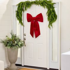 a white door with a red bow hanging on it's side next to a potted plant