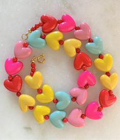 "Kids Brite Multi Colored Plastic Heart Necklace with Red Mini Spacer Beads Gold Tone Spring Ring Clasp Closure Brite Multi Hearts are Red, Hot Pink, Pink, Aqua, Yellow Hearts Measure 5/8\" Wide Necklace Measures 15\" Imported COMPLIMENTARY DOMESTIC SHIPPING" Multicolor Beaded Jewelry For Valentine's Day, Playful Heart Beads For Jewelry Making, Multicolor Double Heart Jewelry For Valentine's Day, Colorful Heart-shaped Round Beads Jewelry, Valentine's Day Jewelry With Heart-shaped Beads, Valentine's Day Jewelry With Heart Beads, Valentine's Day Multicolor Beaded Jewelry, Valentine's Day Playful Beaded Jewelry, Valentine's Day Multicolor Double Heart Jewelry