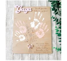 a wooden plaque with handprints on it next to some green leaves and flowers