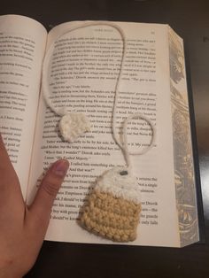 a hand is holding an open book with a crocheted item on it