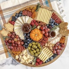 a platter filled with different types of cheeses, fruits and crackers on top of a checkered table cloth