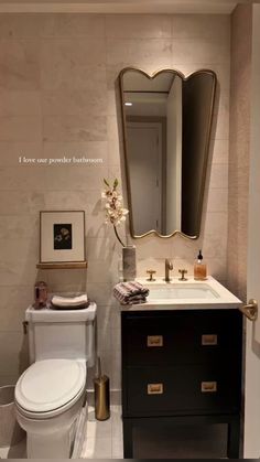 a white toilet sitting next to a sink in a bathroom under a large framed mirror