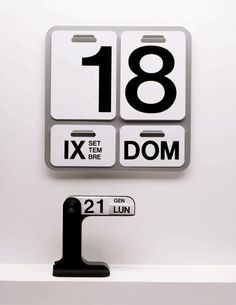 a white and black clock sitting on top of a shelf next to a number sign