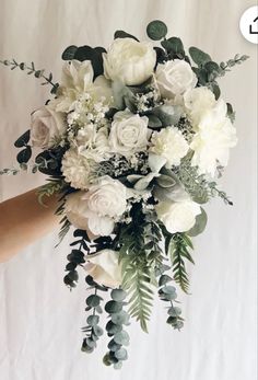 a person holding a bouquet of white flowers and greenery in front of a tweep