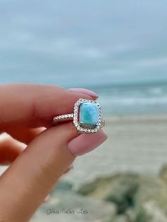 a woman's hand holding a ring with a blue stone in it