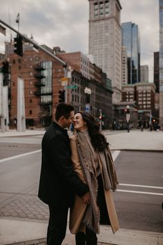 a man and woman standing next to each other on a sidewalk in front of tall buildings