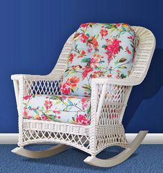 a white wicker rocking chair against a blue wall with flowers on the seat and back