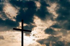 a cross is silhouetted against a cloudy sky