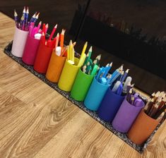 a row of colored pencils sitting on top of a wooden table next to a mirror