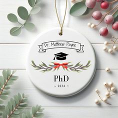 a personalized ornament with a graduation cap and ribbon on it next to greenery