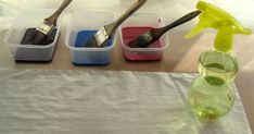 three plastic containers filled with different types of paint and brushes on top of a table