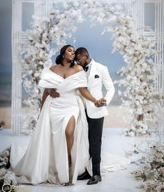 a man and woman in formal wear standing next to each other under an archway with white flowers