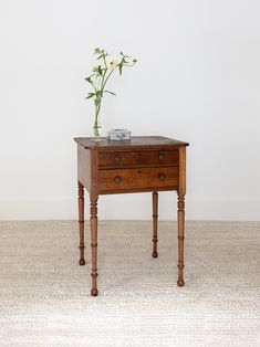 a small wooden table with two drawers and a flower in it on the floor next to a white wall