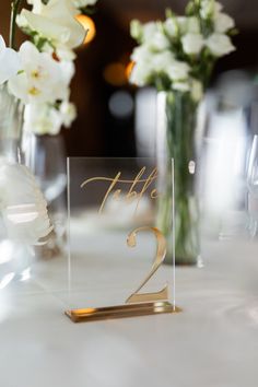 the table numbers are placed in glass vases with white flowers behind them and on top of each other