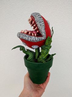 a hand holding a fake tomato with teeth on it's head and green plant