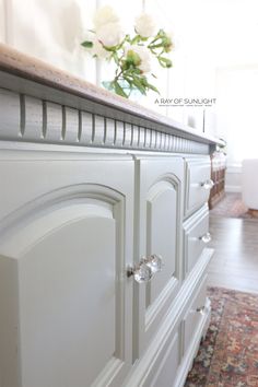 a close up of a white dresser with flowers in the vase on top and an area rug