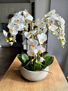 white orchids are in a bowl on a wooden counter top, with green leaves