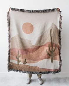 a woman is holding up a blanket with cactus and sunsets in the sky on it