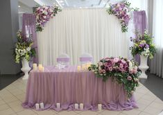 the table is set up with purple and white flowers, candles, and napkins