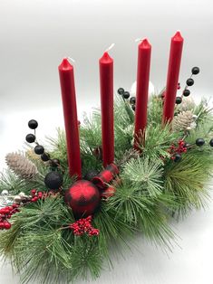 a group of candles sitting next to each other on top of a christmas wreath with pine cones and berries