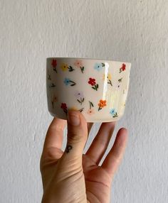 a hand holding up a white cup with flowers on the outside and inside, in front of a white wall