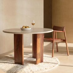 a round table with two wooden chairs and a bowl of fruit on it in front of a wall