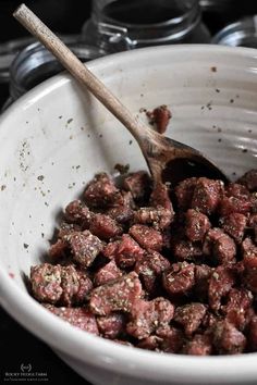 a white bowl filled with meat next to a wooden spoon