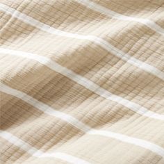 an unmade bed with white and beige plaid sheets