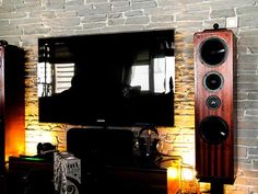 a flat screen tv sitting on top of a wooden stand next to speakers and a brick wall