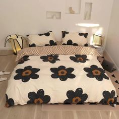 a bed with black and white flowers on it in a room that has wood floors