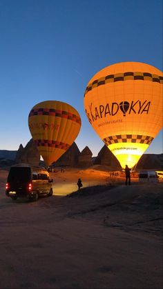 three hot air balloons in the sky over some cars and people standing near by at dusk